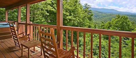 Una terraza de madera con sillas y vistas a una cadena montañosa boscosa.