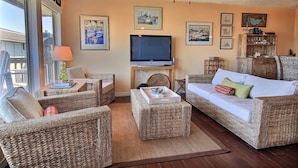 A living room with wicker furniture, a television, and framed pictures on the wall. - Amazing sunrise views, swimming pool, boardwalk to the beach, picnic tables, pla (Port Aransas)