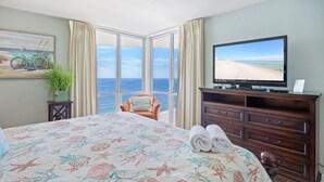 Een hotelkamer met een groot bed, een televisie, uitzicht op de oceaan en een houten dressoir.