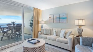 Een woonkamer met een bank, een salontafel en een lamp. Door een schuifdeur is er uitzicht op de oceaan.