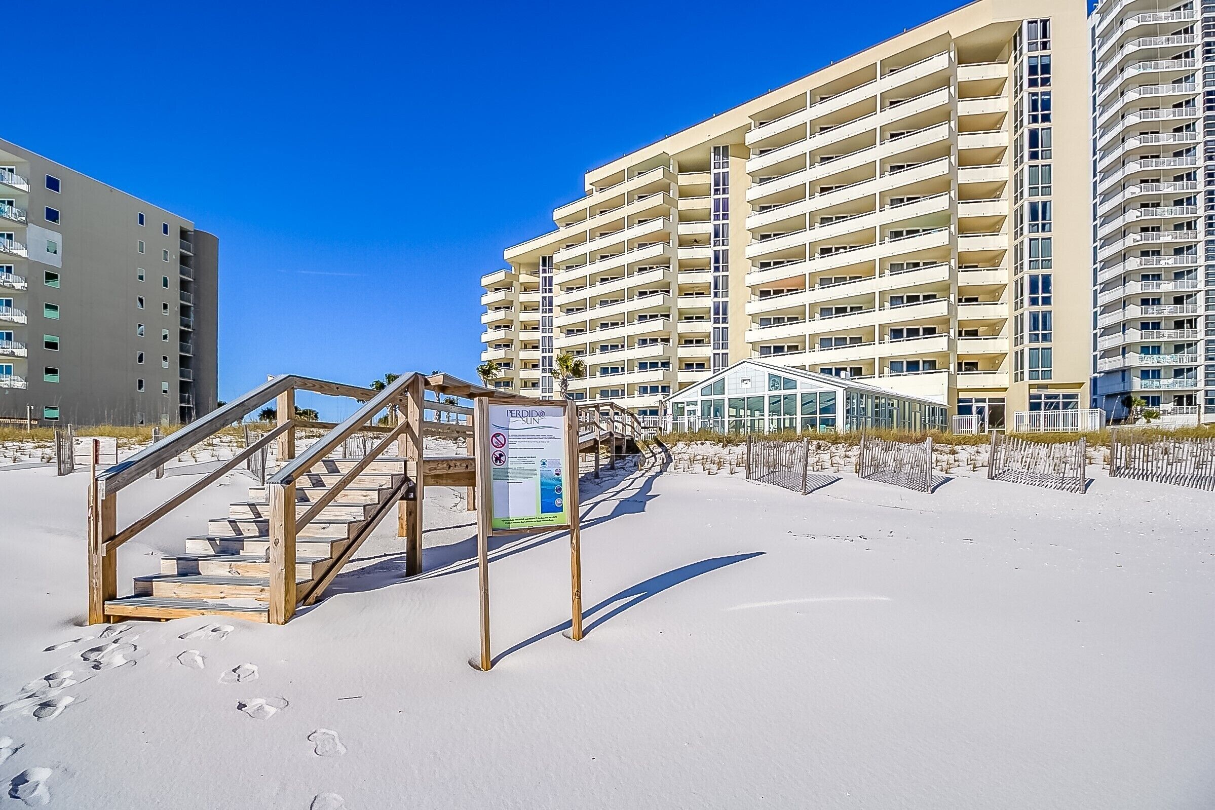 Un hôtel situé en bord de mer, doté d’un escalier en bois menant à une zone abritée, le tout entouré d’immeubles de grande hauteur.