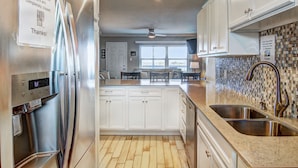 A modern kitchen with stainless steel appliances, white cabinetry, a granite countertop, and a tiled backsplash. - This wonderful condo is located on the 2nd floor of the beachfront building in f (Port Aransas)