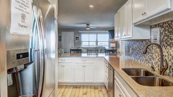A modern kitchen with stainless steel appliances, white cabinetry, a granite countertop, and a tiled backsplash.