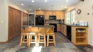 Una cocina moderna con armarios de madera, una isla central con taburetes, un refrigerador, microondas y lavavajillas.