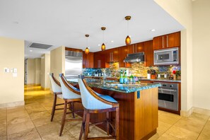 A modern kitchen with a central island, bar stools, stainless steel appliances, and wooden cabinetry. - Honua Kai | Ocean View (Partial) 3 BR | Free Car w/ 6+ Nights | HKH-150 (Lahaina)