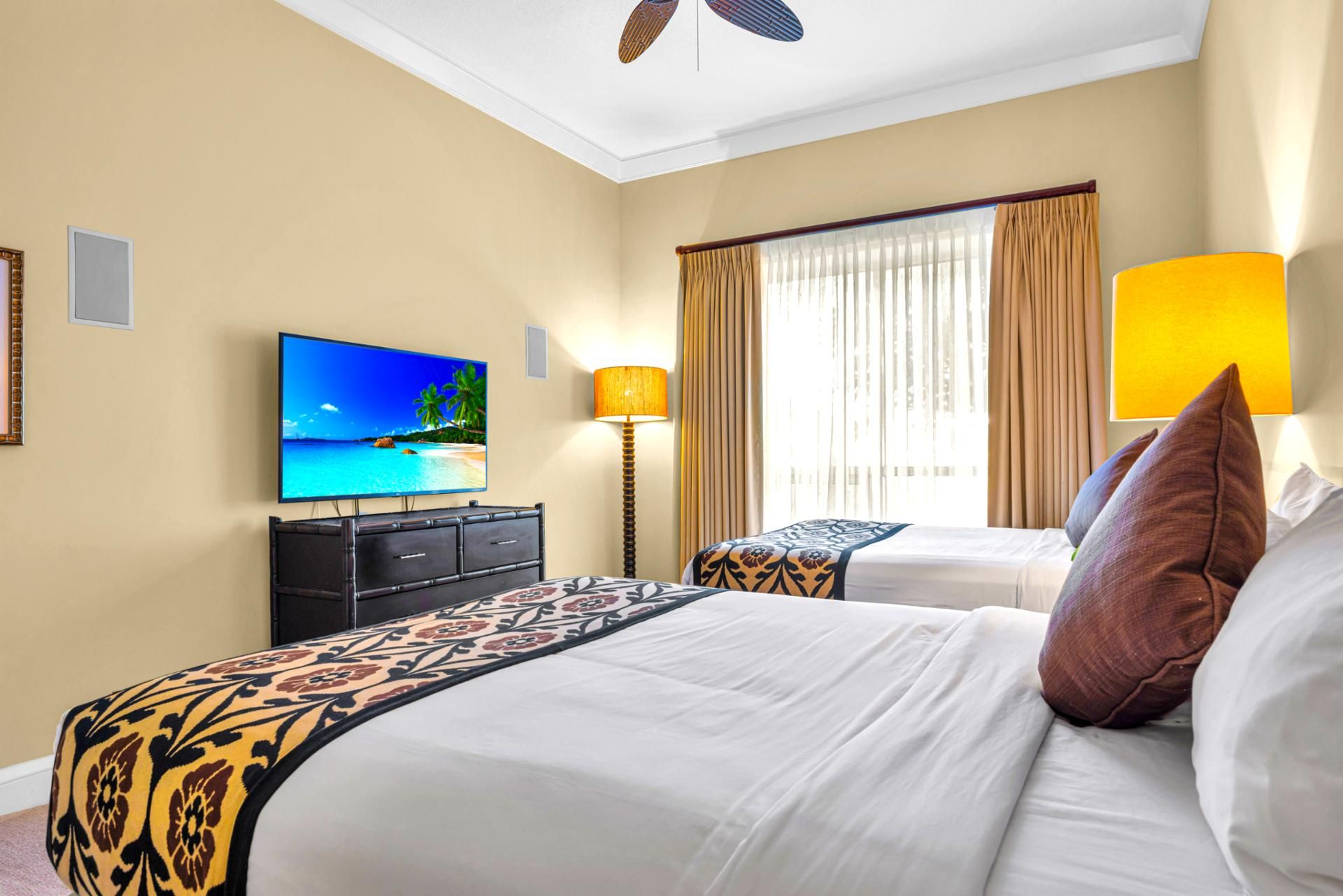 A hotel room with a bed, a TV displaying a beach scene, a desk, and a lamp.