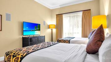 A hotel room with a bed, a TV displaying a beach scene, a desk, and a lamp.