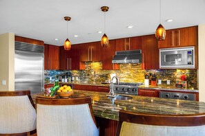 Une cuisine moderne avec des meubles en bois, un réfrigérateur en acier inoxydable, un four à micro-ondes encastré, une cuisinière à gaz et des luminaires suspendus.