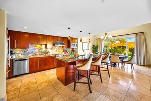 Una cocina moderna con armarios de madera, un refrigerador de acero inoxidable y una isla central con taburetes de bar.