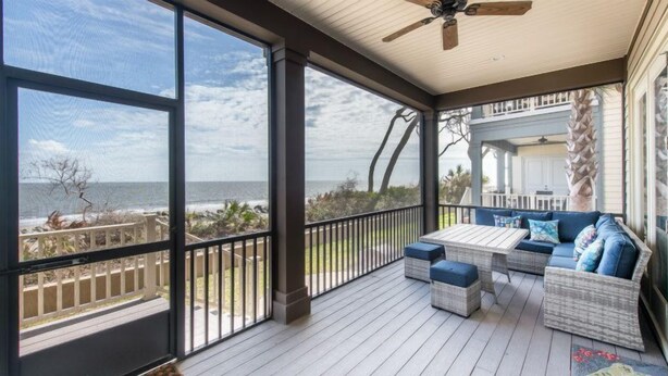 A covered deck with a view of the ocean, featuring a seating area with cushions and a table. - Ocean Cottage 51 The Colorful Cottage The Cottages at Jekyll Oceanfront (Jekyll Island)