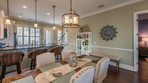 A dining area with a wooden table, cushioned chairs, and a decorative centerpiece. - Ocean Cottage 51 The Colorful Cottage The Cottages at Jekyll Oceanfront (Jekyll Island)