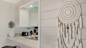 A kitchen with a white countertop, a sink, a coffee maker, and a white dreamcatcher hanging on the wall. - 🌴 Islander #107 “Good Vibrations” – Your Easy, Fun Beach Getaway! 🌊 (Destin)