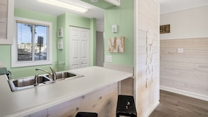 A kitchen with a white countertop, stainless steel sink, and a window with blinds. - 🌴 Islander #107 “Good Vibrations” – Your Easy, Fun Beach Getaway! 🌊 (Destin)