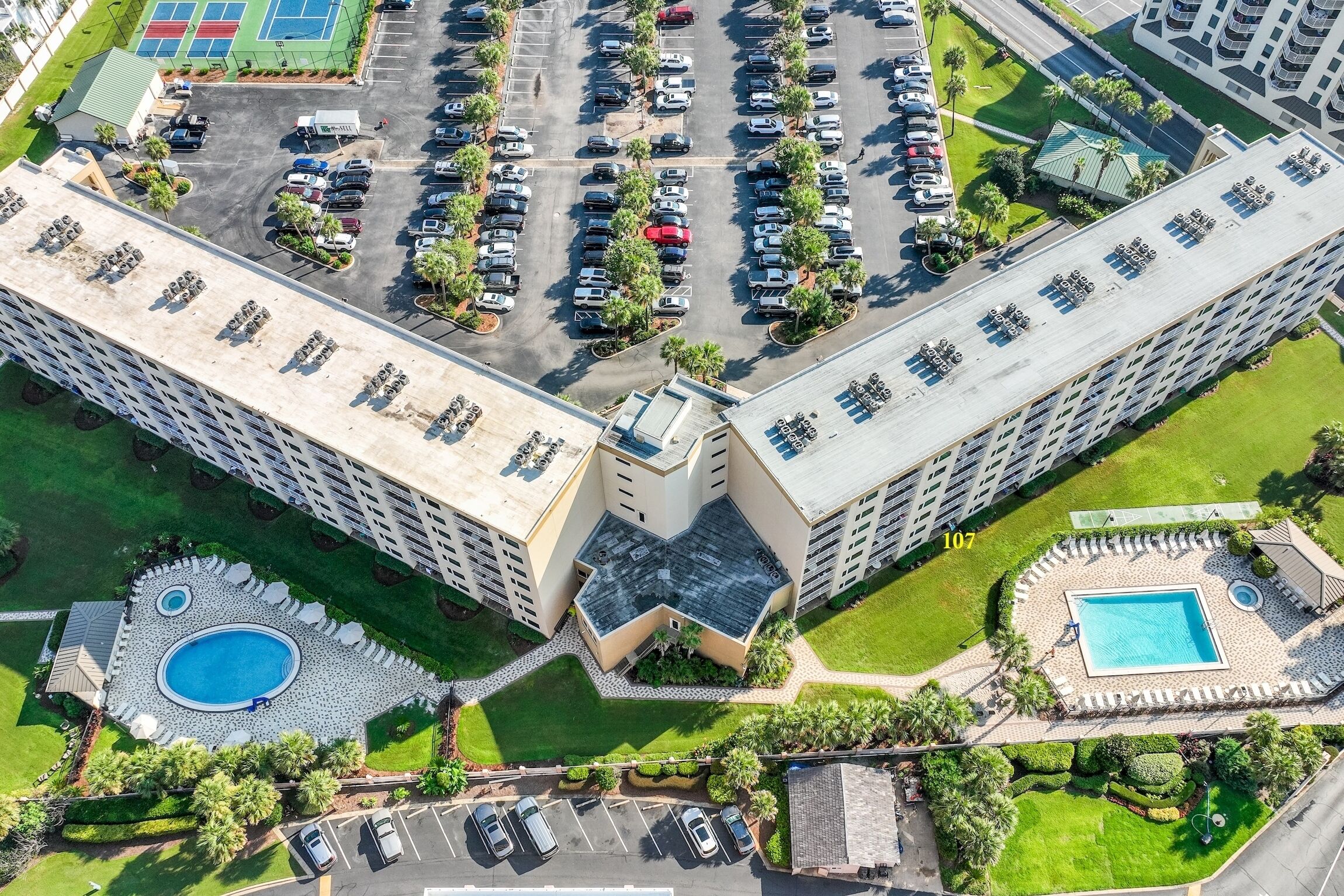 An aerial view of a hotel with multiple parking lots, a swimming pool, and landscaped areas.