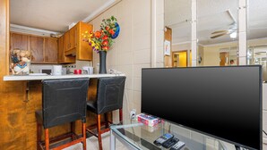 Una cucina moderna con mobili impiallacciati in legno, una zona pranzo con due sedie nere, un tavolino da caffè in vetro e una TV a schermo piatto su un mobile.