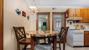 Zona pranzo con tavolo rotondo, quattro sedie di legno e un piano in marmo. In cucina, si trova uno sgabello bianco e mobili in legno.
