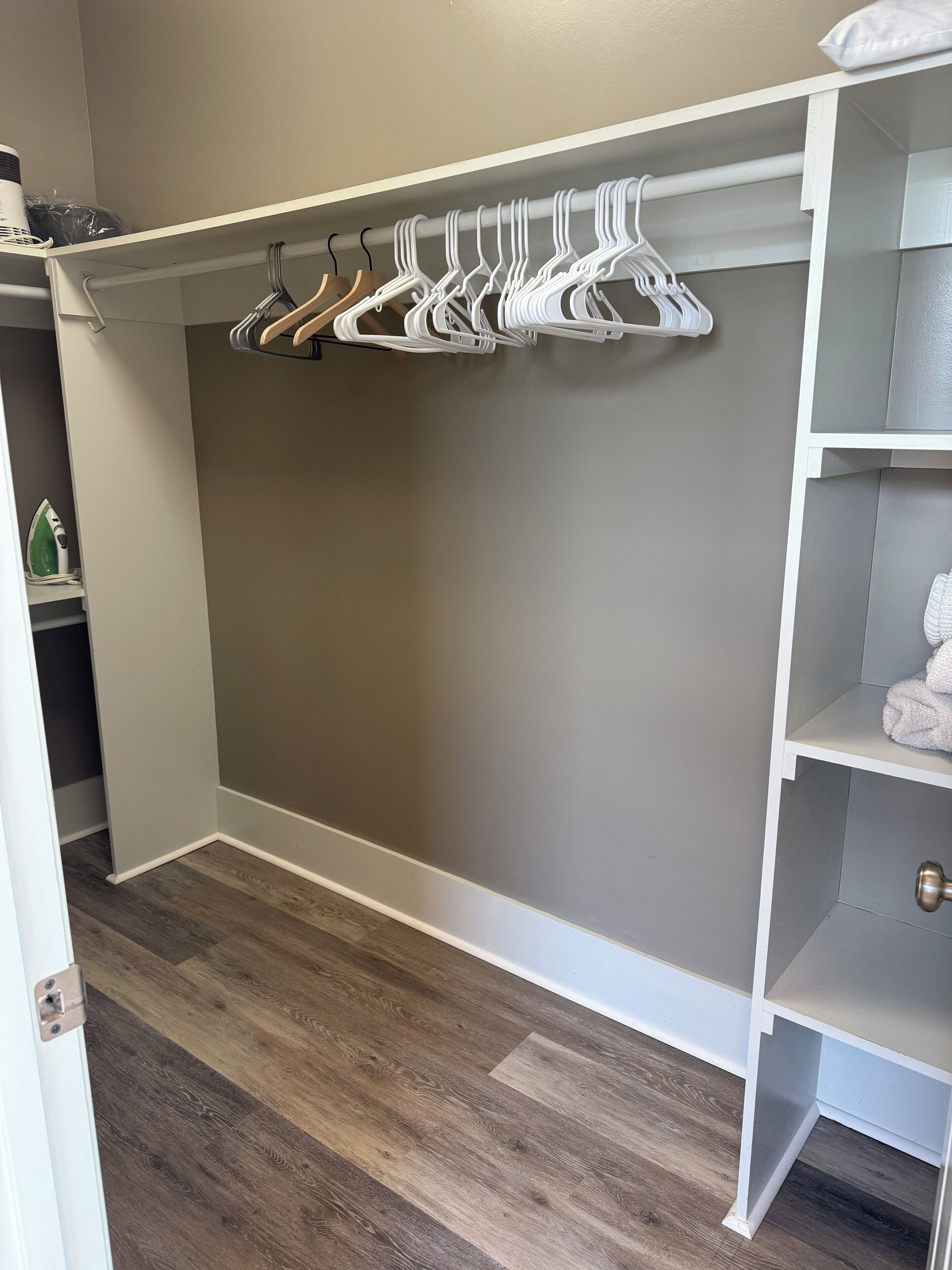 Un vestidor con pared gris, suelo de madera y una barra blanca para colgar ropa con varios perchas blancas.