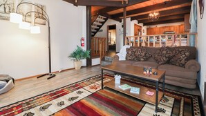 Una sala de estar acogedora con techo de madera, un sofá, una mesita de centro y una escalera que sube a un nivel superior.