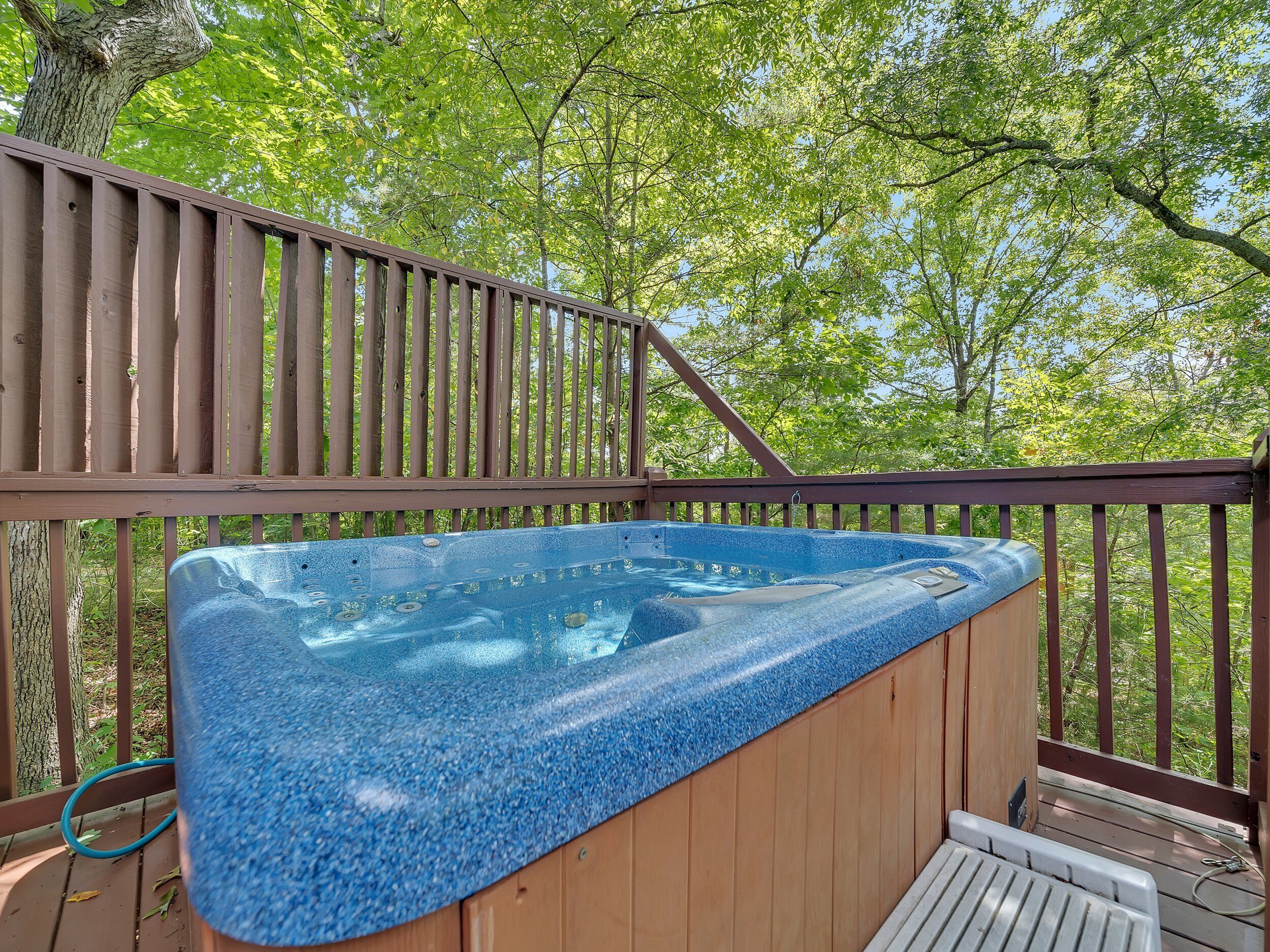 Un jacuzzi en una terraza de madera con vista a árboles.