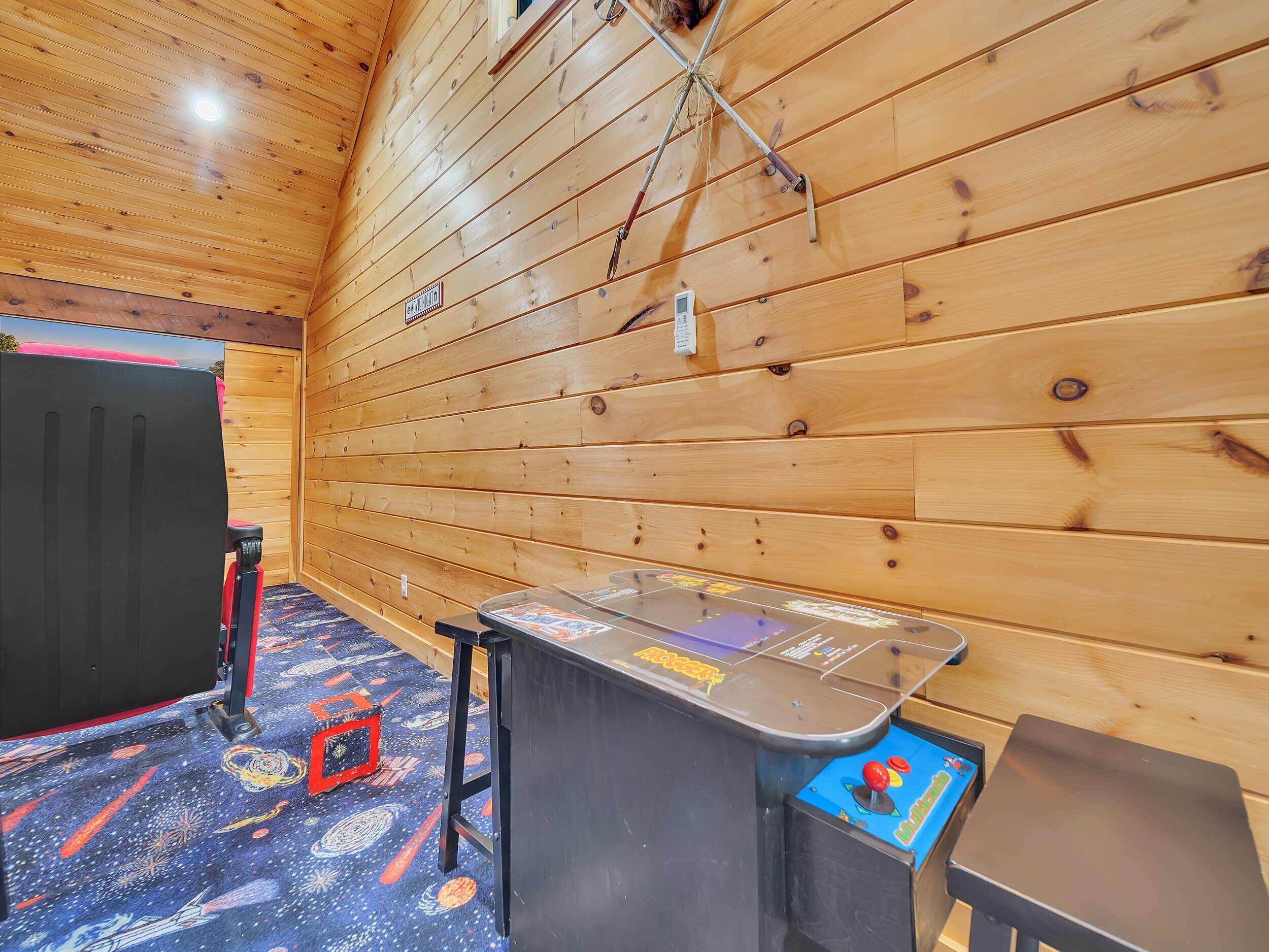 Un interior de madera con proyector en el techo, una mesa con un juego y una silla roja.