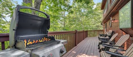 A barbecue grill on a wooden deck with chairs and a building in the background.