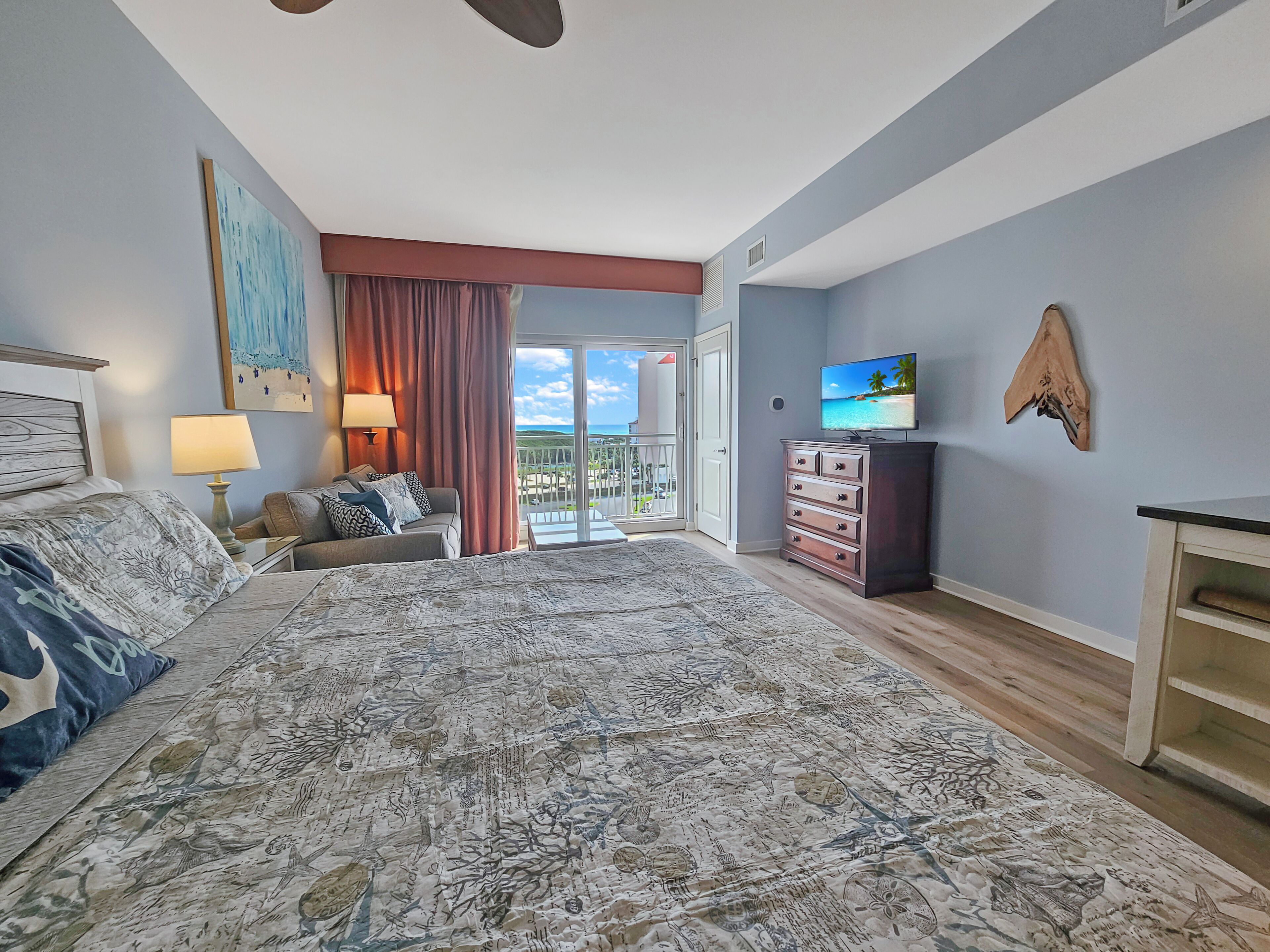 A bedroom with a large bed, a television, a dresser, and a balcony with a view.