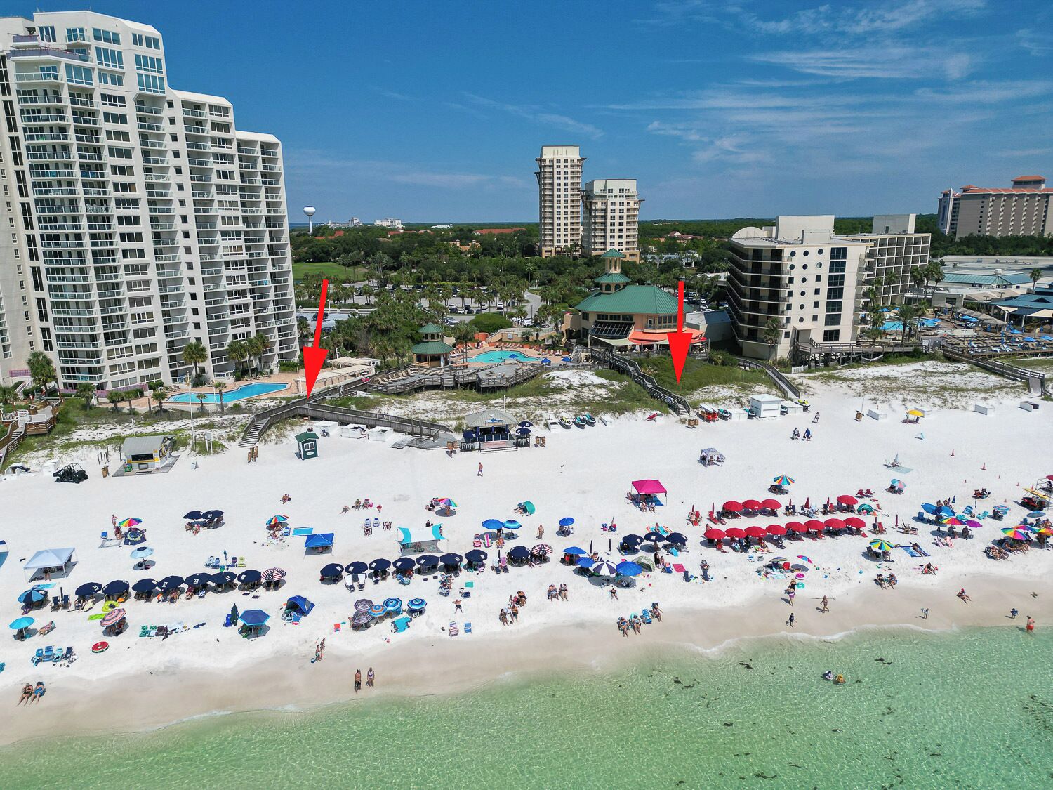 A beach resort with multiple high-rise buildings, a central pool area, and numerous beach umbrellas.