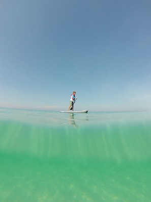 A person paddleboarding on a calm, turquoise sea under a clear sky.