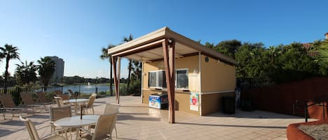 Un espacio al aire libre con mesas y sillas, un quiosco techado y vista a un cuerpo de agua.