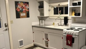 Une cuisine avec des meubles blancs, une cuisinière et un évier. Il y a un tapis sur le sol et un tableau au mur.