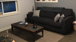 Un salon avec un canapé de couleur sombre, une table basse en bois, un vase décoratif et un tableau encadré accroché au mur.