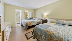 Ein Hotelzimmer mit zwei Betten, einem begehbaren Kleiderschrank, einem Badezimmer mit Dusche und einem Spiegel.