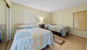 Een slaapkamer met twee bedden, een nachtkastje, een lamp en een raam met zonwering.