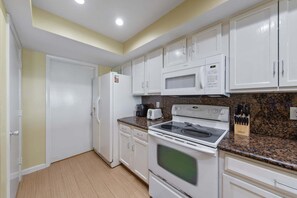 A kitchen with white cabinets, a microwave, a stove, and a refrigerator. - Edgewater 104 Ground Floor! Pool Heated during Colder Months! (South Padre Island)