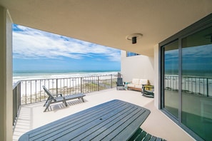 A balcony with a view of the beach, a table, a chair, and a sofa.