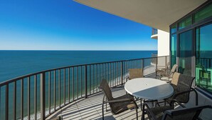 Un balcón con una mesa redonda y sillas, con vista a un mar azul y despejado.
