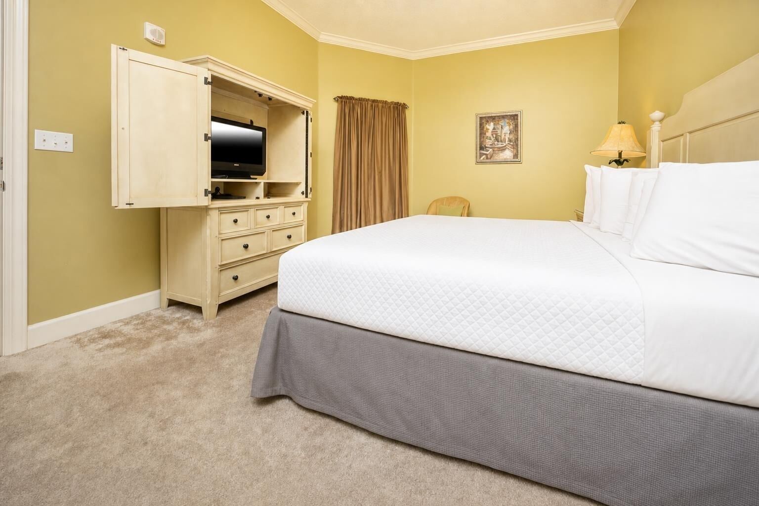 Una habitación de hotel con una cama, un aparador, un televisor, una lámpara y un cuadro en la pared.