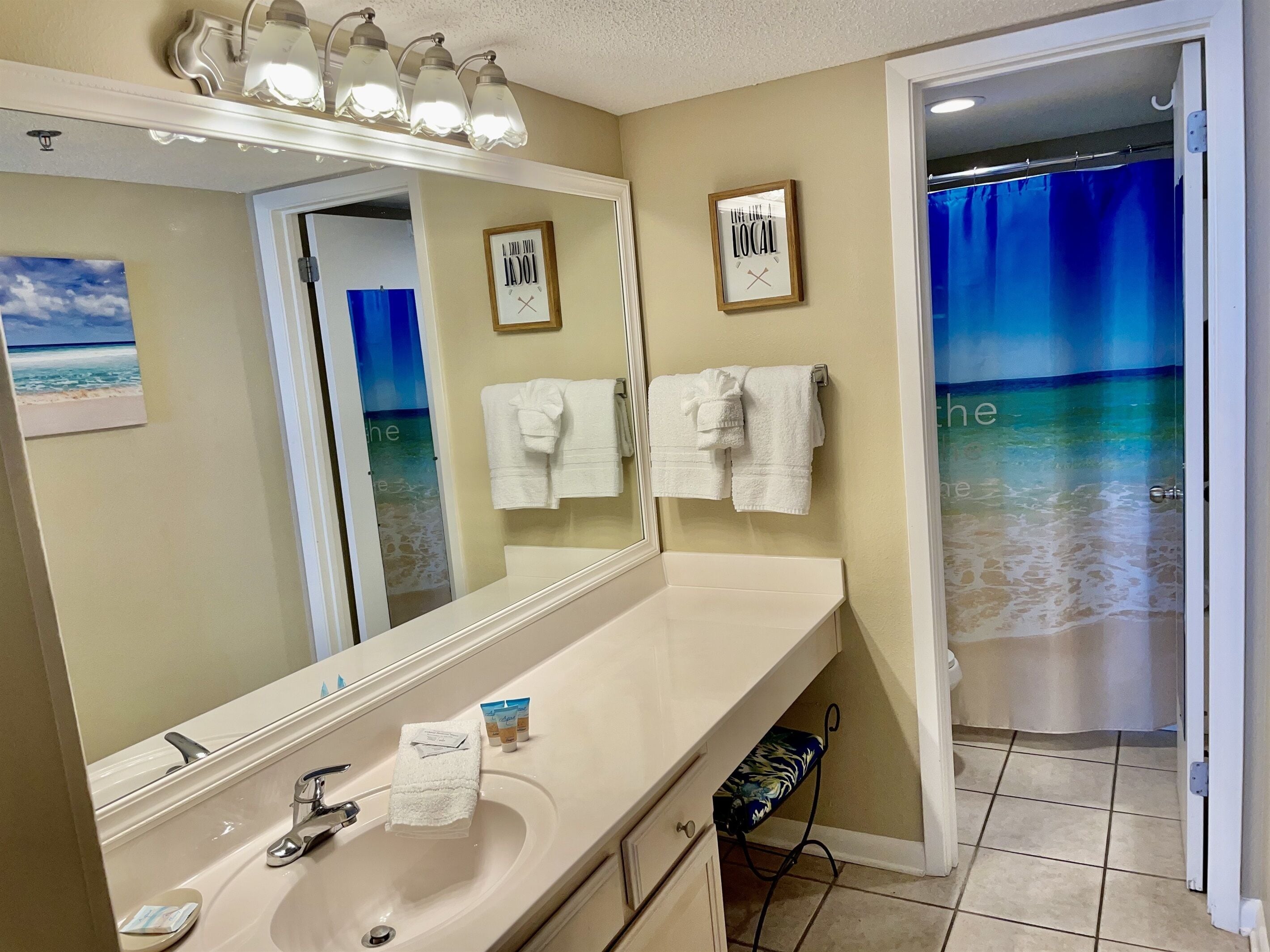 A bathroom with a large mirror, a sink, and a shower curtain with a beach view.