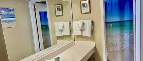 A bathroom with a large mirror, a sink, and a shower curtain with a beach view.
