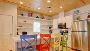 A kitchen with white cabinets, a stainless steel refrigerator, a microwave, and a coffee maker. There are colorful chairs around the kitchen island. - You are certainly Shore To Love It! This fabulous island style home is located r (Port Aransas)