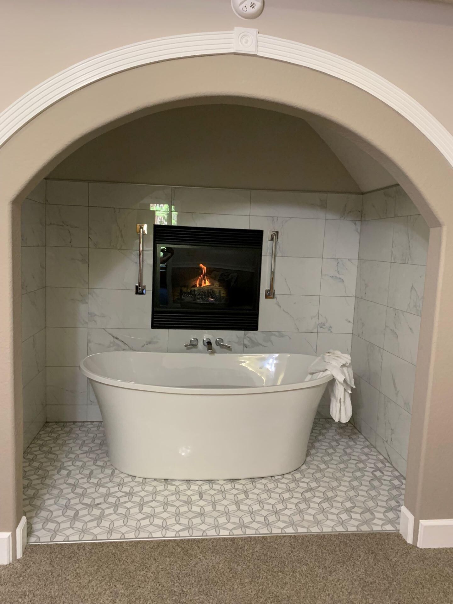 A bathroom with a freestanding bathtub, a fireplace, and a handrail.