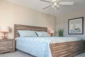 Un dormitorio con una cama de madera, dos mesitas de noche, un ventilador de techo y un cuadro enmarcado en la pared.