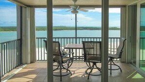 Un balcon avec une table et des chaises, un ventilateur de plafond et une vue sur une étendue d’eau.