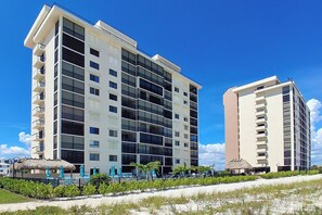 Un hotel de varios pisos con balcones, un área de piscina con sombrillas y ubicación frente a la playa.