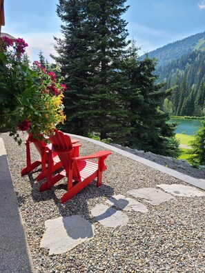 Un espace aménagé avec des fauteuils Adirondack rouges et un pot de fleurs, offrant une vue sur un lac et des montagnes boisées.