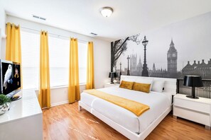 A modern bedroom with a large bed, a flat-screen TV, and a cityscape mural on the wall. - 3BR Townhouse near Cay Lake & Epic Universe (Orlando)