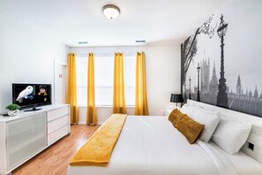 A hotel room with a bed, a television, a window with curtains, and a wall with a cityscape mural.