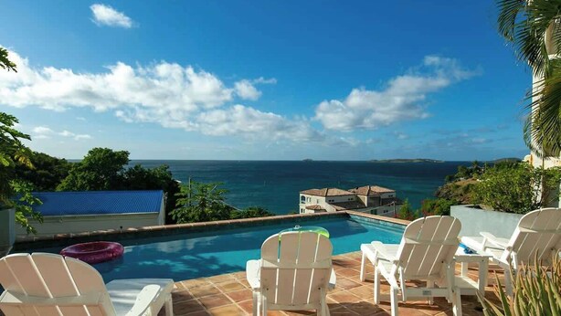 A pool area with white chairs and a view of the ocean.