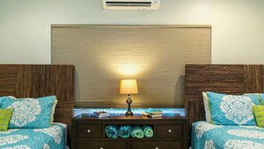 A hotel room with two beds, a nightstand with a lamp, and a wall-mounted air conditioner.