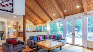Un'ampia zona giorno con soffitto in legno, ampie finestre e un tavolo da caffè centrale.